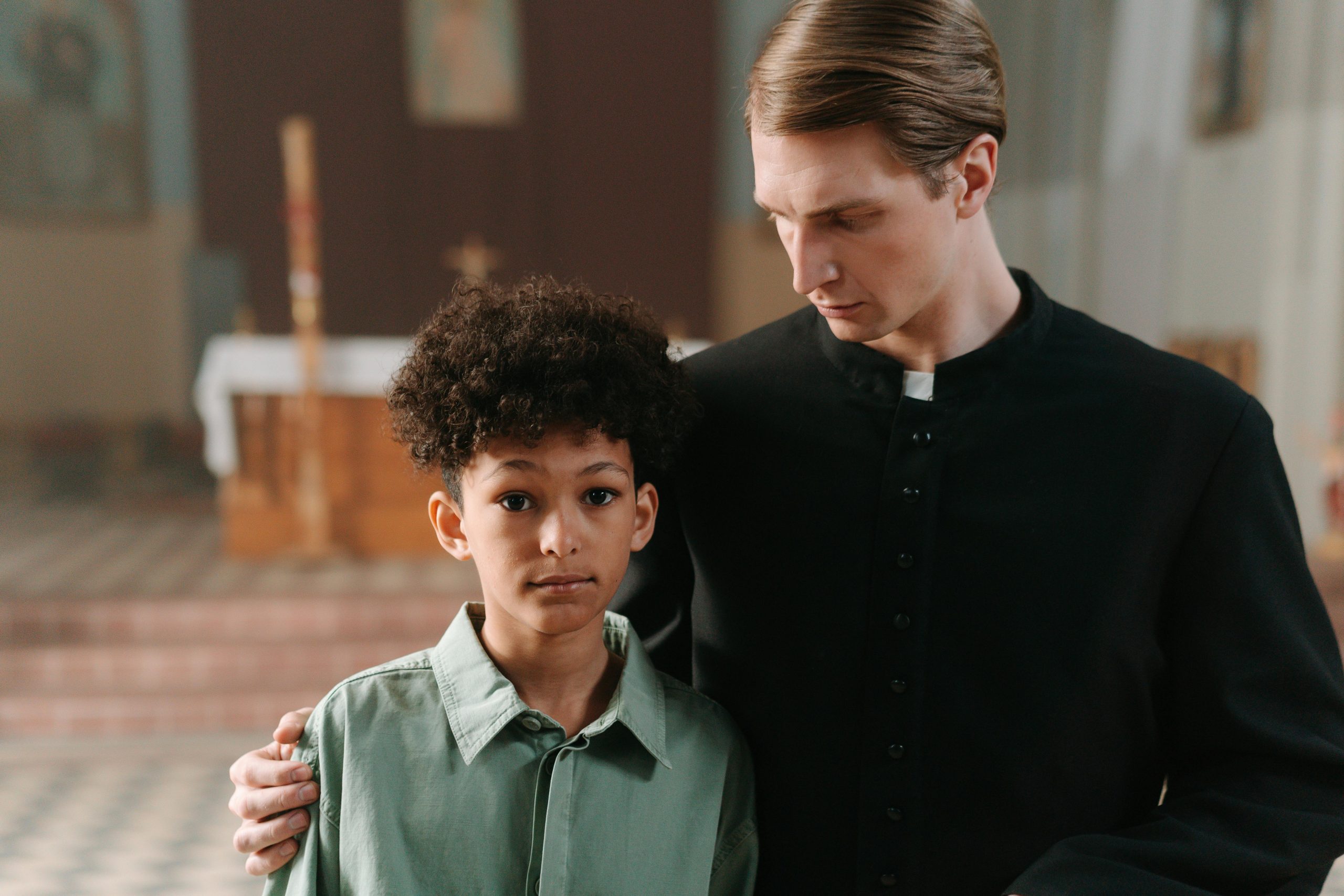 A priest and child standing closely inside a church, conveying peace and comfort.
